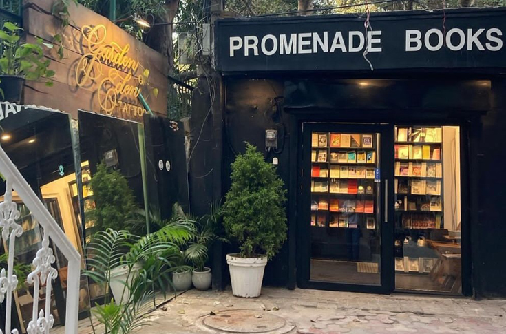 Interior of Promenade Books, an independent bookstore in Hauz Khas Village, Delhi, featuring black shelves filled with rare and unconventional books, vinyl records, handwritten notes, vintage decor, and a cosy artistic atmosphere curated by young booksellers passionate about literature, music, and underground culture