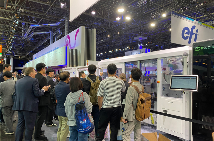 EFI exhibition stand demonstrating single-pass printing innovations including Packsize EFI X5 Nozomi automated box system, Nozomi 14000 SD and AQ printers, Nozomi 12000 MP, and Reggiani BOLT XS textile printer showcasing packaging and display applications