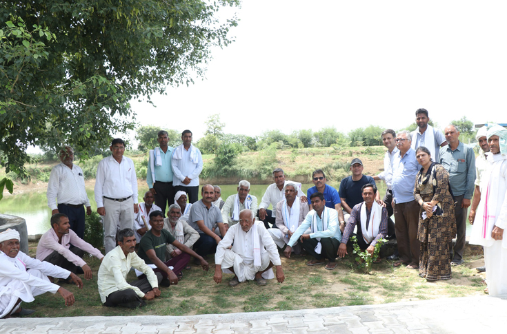 Restored village pond in Dhaki under Siegwerk India CSR project showing de-silted water body, recharge shafts, greenery, medicinal plant plantation, fish stocking, and community recreational space with benches and gazebo