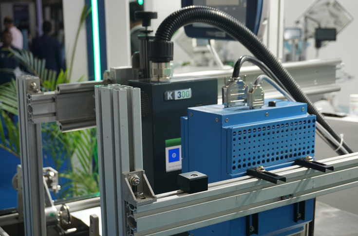 Domino K300 industrial inkjet printing system demonstrating high-speed variable data printing on pharmaceutical packaging materials like cartons and blister foils at a trade exhibition