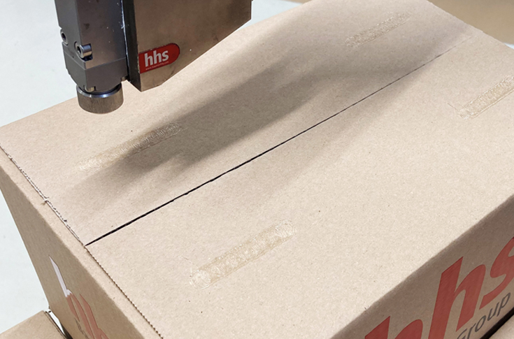 Baumer hhs pallet stabilisation system applying anti-slip hot melt adhesive on stacked boxes to secure loads for transport without plastic wrap