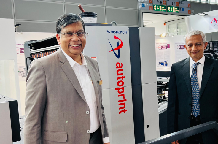 Autoprint team at Drupa showcasing the Finecoat 105-Drip Off UV coating machine while engaging with international visitors and discussing packaging industry trends and global business expansion
