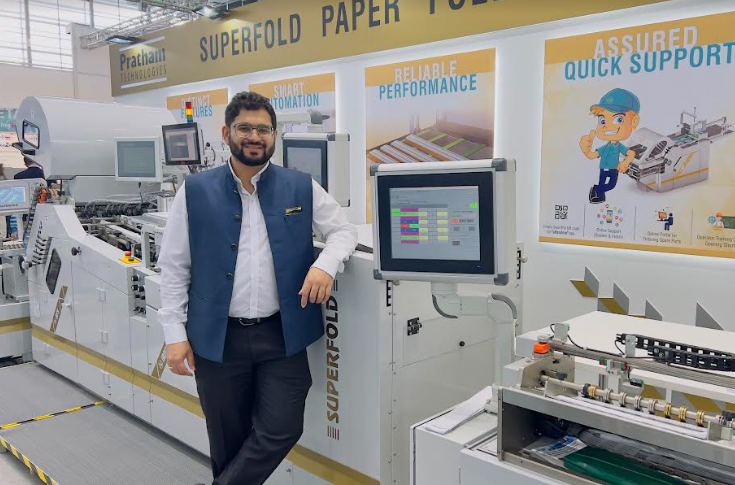 Pratham iRPF 53 automated folding and tray packing machine displayed at Drupa exhibition, featuring robotic system, creasing pre-setter, and super tray packer for high-speed packaging and quality control